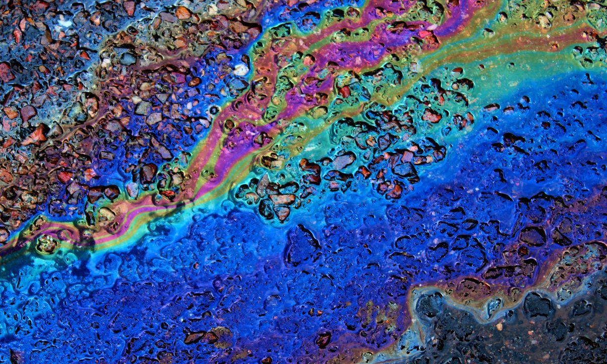 An oil slick on wet pavement spreading into bands of blue, green, and violet