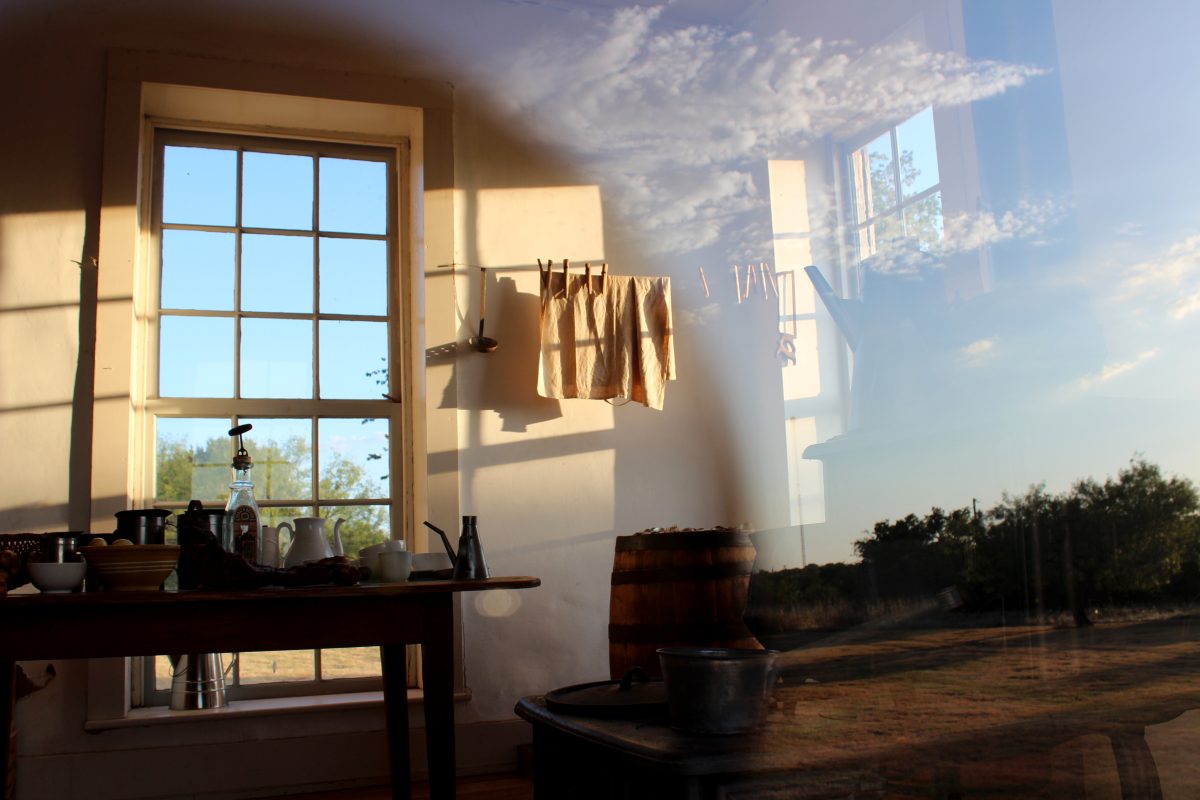 Sunlit historic kitchen seen through old window glass, sky reflected in the pane