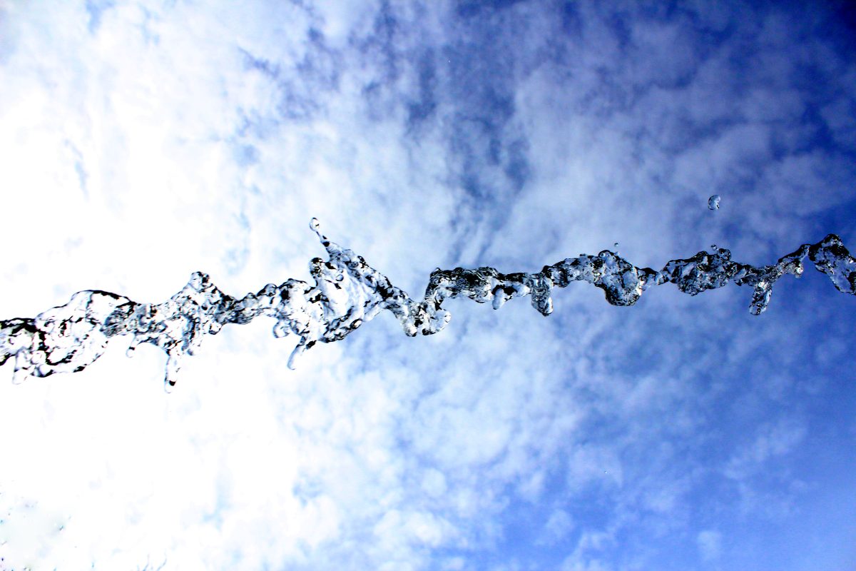 An arc of water frozen mid-air against a blue sky and scattered clouds