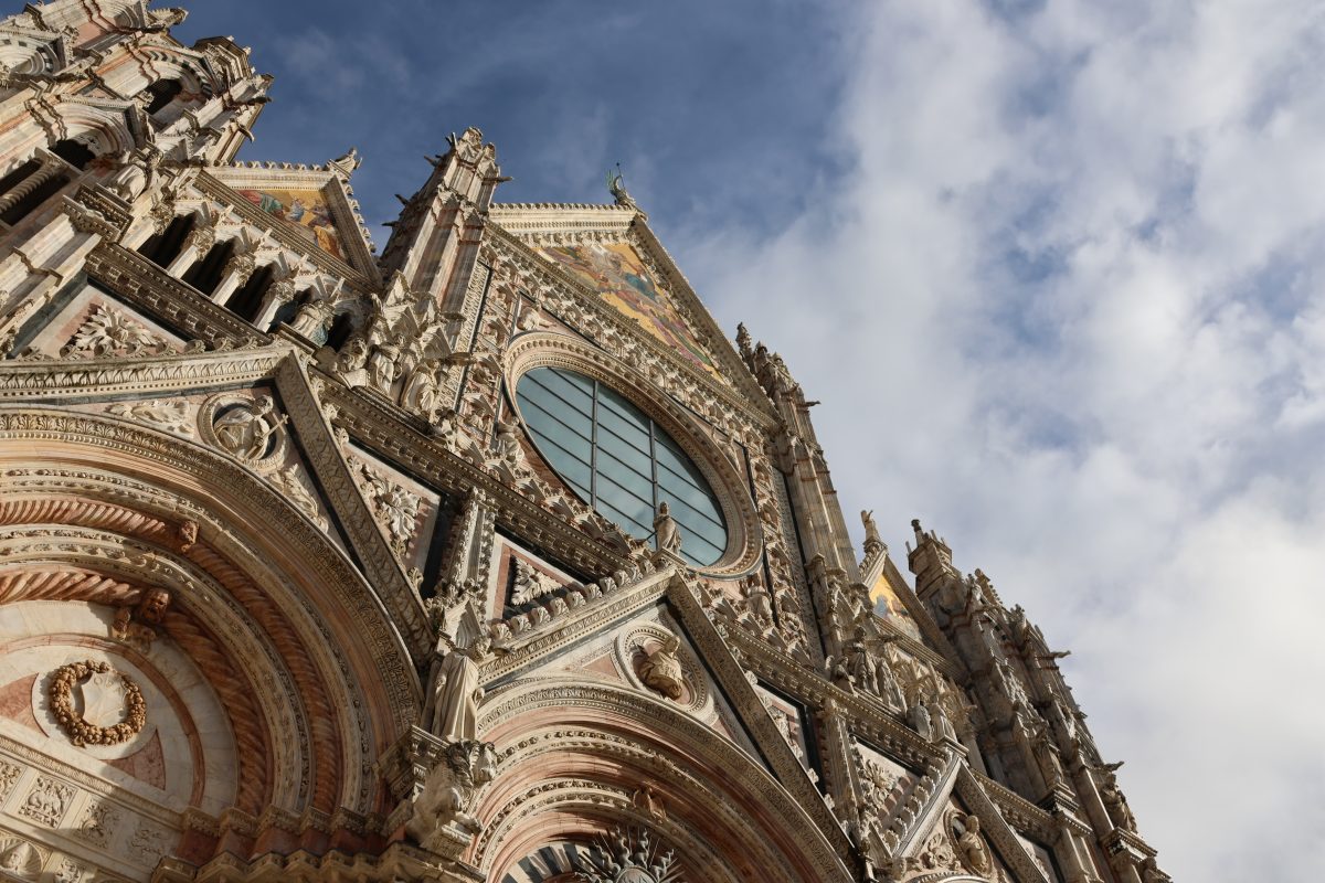 The carved marble facade of Siena Cathedral against a cloudy sky
