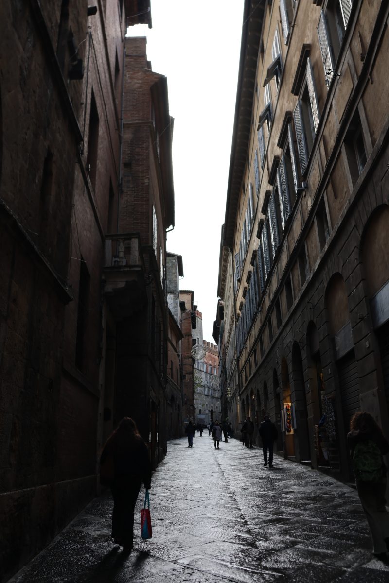 A narrow Italian alley in the rain, figures walking in the distance