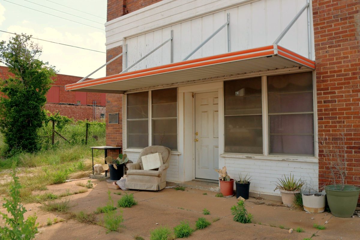 A worn storefront porch with an armchair beneath an orange awning